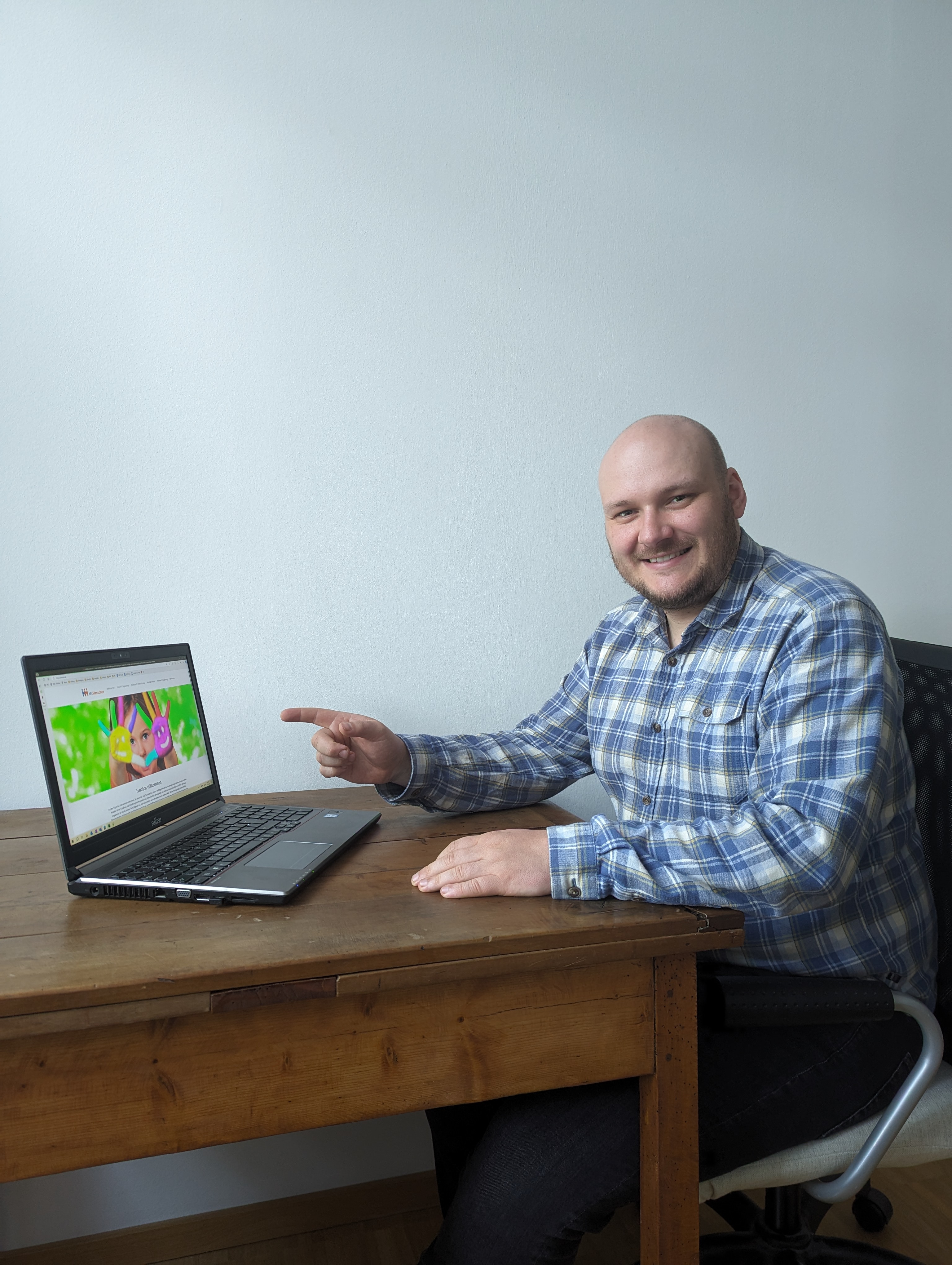 Ein Mann sitzt an einem Tisch und zeigt auf einen Laptop
