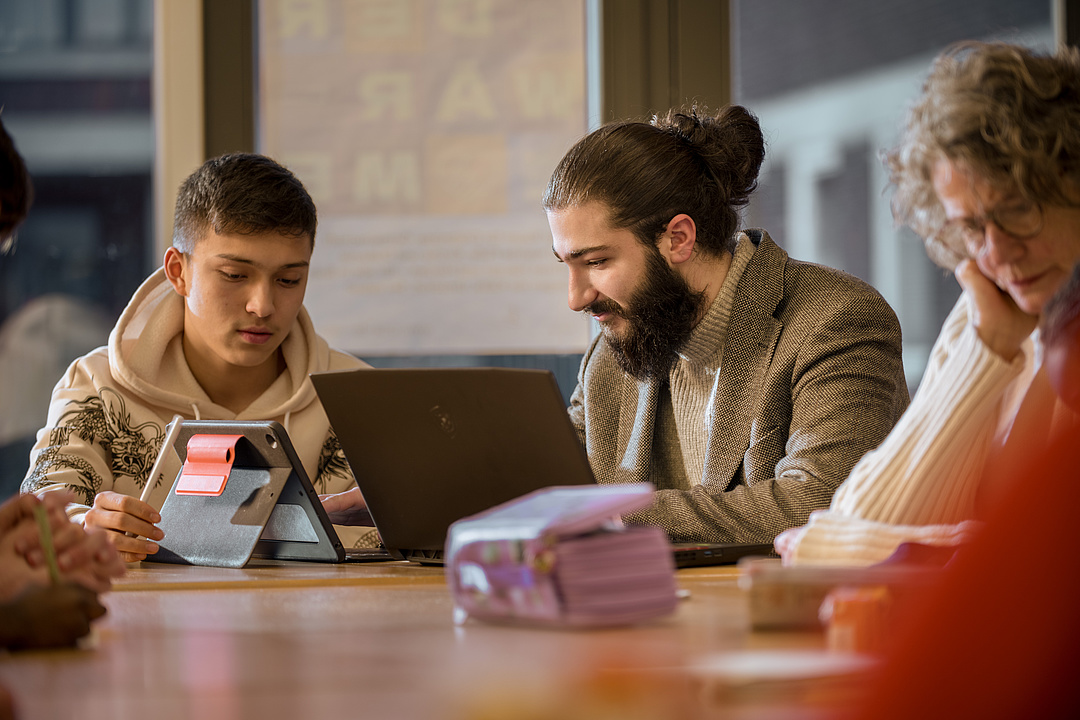Ein junger Mann und ein kleiner Junge sitzen am Tisch und unterhalten sich. Sie haben einen Laptop bei sich.