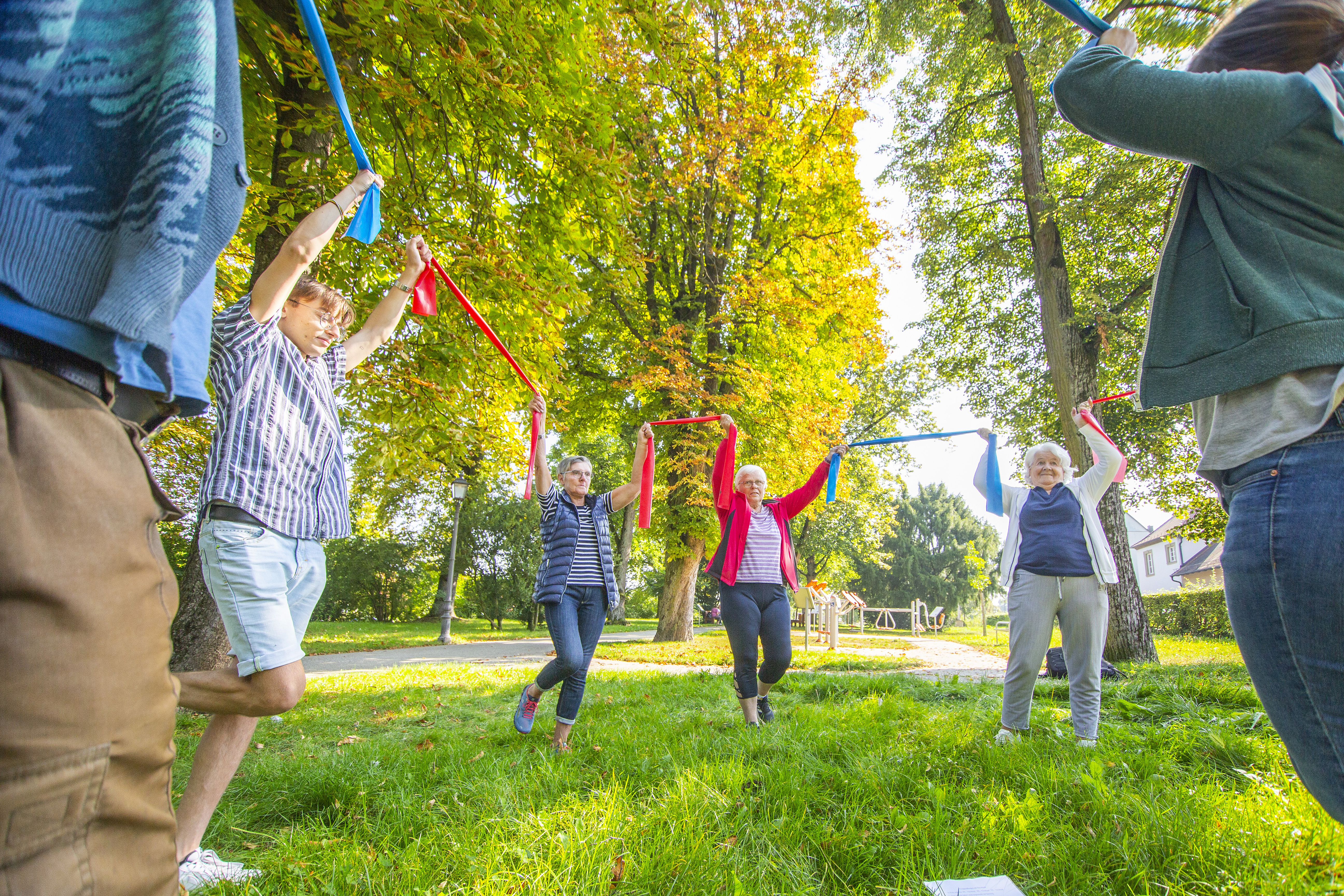 Mehrere Menschen bewegen sich mit Bändern in einem Park.