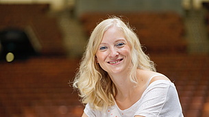 Eine blonde Frau sitzt in einem Saal und lächelt in die Kamera. Es ist Fenja Grieshammer, die sich ehrenamtlich im Mehrgenerationenhaus Wunsiedel engagiert. 